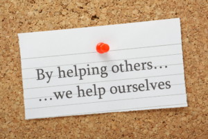 Sign pinned to a bulletin board that says By helping others...we help ourselves