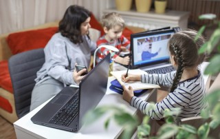 Distant education and work at home, children doing homework, mother working and help them. Elementary school kids during online class with parent working remotely in one room, lockdown, focus on girl
