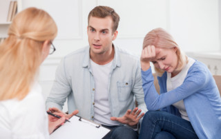 Cheerful young married couple has problems with their relationships. They are sitting and consulting with a psychologist. The woman is crying with desperation. The man is upset