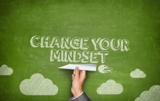 Change your mindset concept on green blackboard with businessman hand holding paper plane
